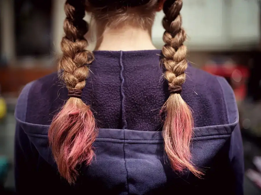 Two long plaits with pink-dyed ends hanging over a navy jumper